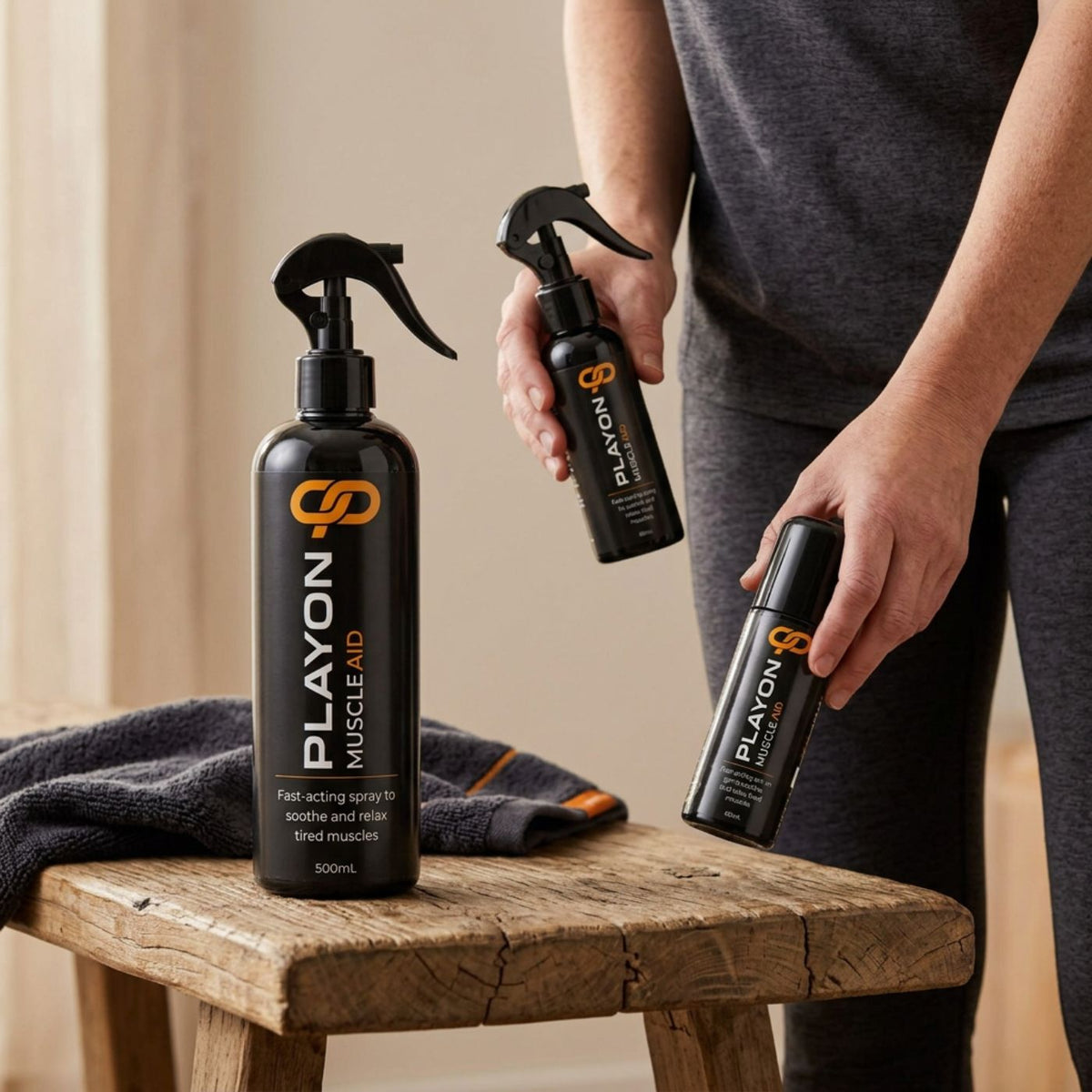 Adult holding PLAYON 80ml spray and 60ml roll-on above a bench beside the 500ml spray