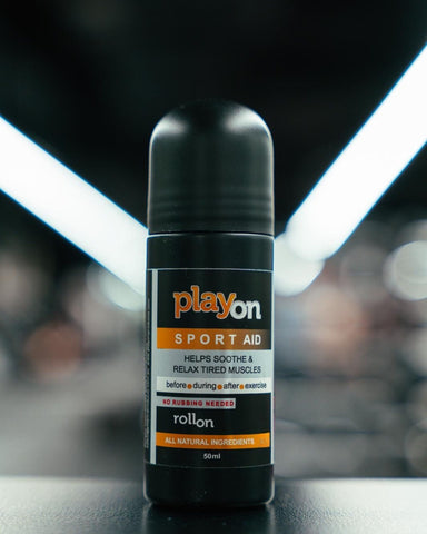 A black roll-on bottle of playon Sport Aid athletic support placed on a dark surface with a blurred gym background and bright overhead lights.